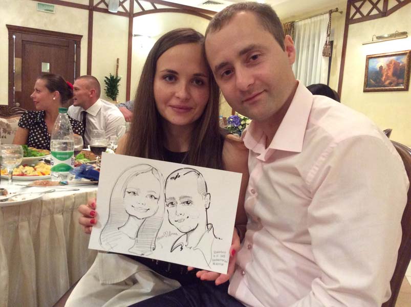 Надя и Дима держат свой шарж на свадьбе